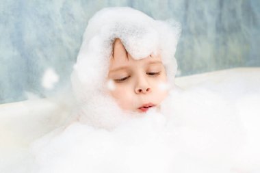 Sabunlu köpüklü bir çocuk banyoda yıkanıyor. Hijyen, temizlik konsepti.