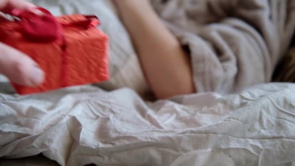 バレンタインデーのコンセプト 男の手はベッドの端に心臓で飾られた贈り物を置く — ストック動画