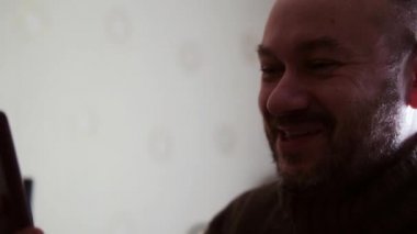 Tıraşsız adam gülümser ve cep telefonundan video yoluyla iletişim kurar..