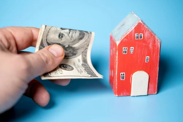 Real estate and money. Wooden toy house and one hundred dollar bill on a blue background. Savings for home construction, mortgage, rental housing concept.