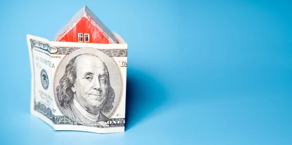 Real estate and money. Wooden toy house and one hundred dollar bill on a blue background. Savings for home construction, mortgage, rental housing concept.