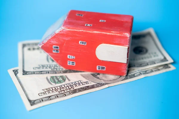 Real estate and money. Wooden toy house and one hundred dollar bill on a blue background. Savings for home construction, mortgage, rental housing concept.