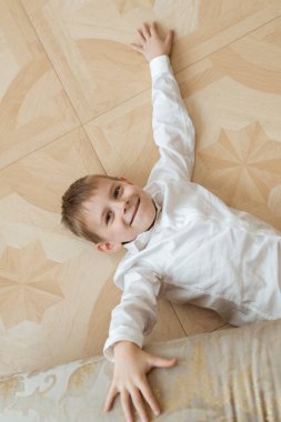 Genç bir çocuk yerde yatıyor. Beyaz gömlekli ve siyah pantolonlu