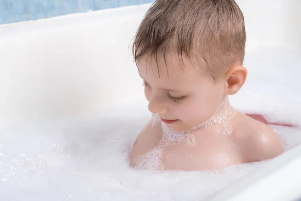 A young boy takes a bath with foam. Personal hygiene for children.