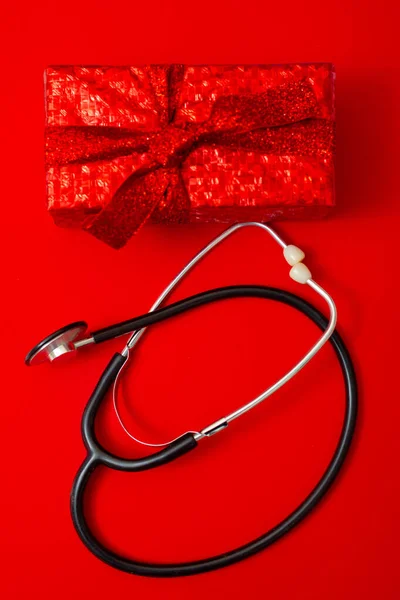 Stethoscope and gift wrapped in red paper on a red background. Health care.