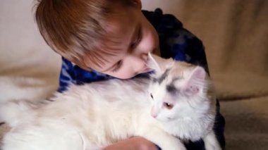 Genç bir çocuk bir kediyi okşuyor. Beyaz kedi yavrusuyla oynuyor..
