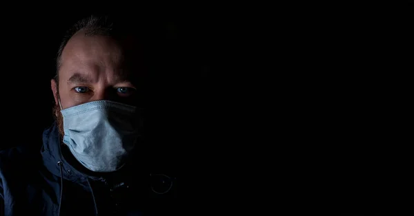 A man in a medical mask on a black background. Lockdown, social quarantine concept. Banner.