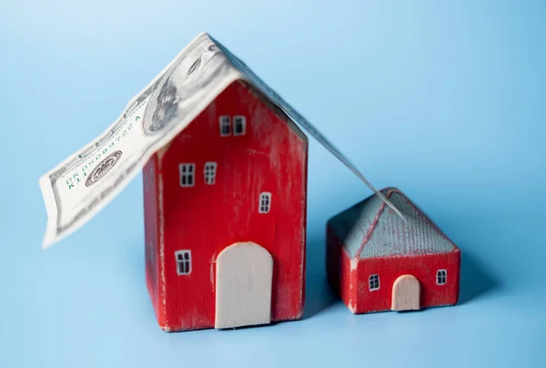 Real estate and money. A hundred dollar bill is like a roof on a toy house. Home insurance, mortgage, rental concept.