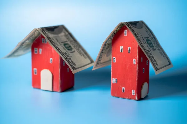 Real estate and money. A hundred dollar bill is like a roof on a toy house. Home insurance, mortgage, rental concept.