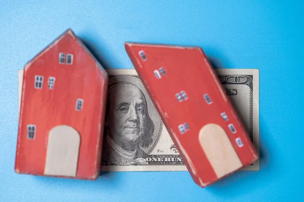 Real estate and money. Wooden toy house and one hundred dollar bill on a blue background. Savings for home construction, mortgage, rental housing concept.