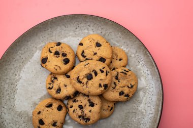 Pembe arka planda bir tabakta çikolatalı kurabiyeler.