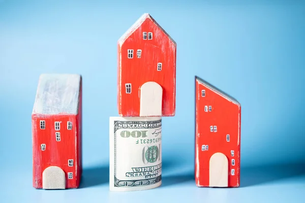 Real estate and money. Wooden toy houses and a hundred dollar bill on a blue background. Savings for home construction, mortgage, rental housing concept.