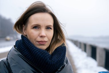 Kışın kalın ceketli orta yaşlı bir kadın kameraya bakar..