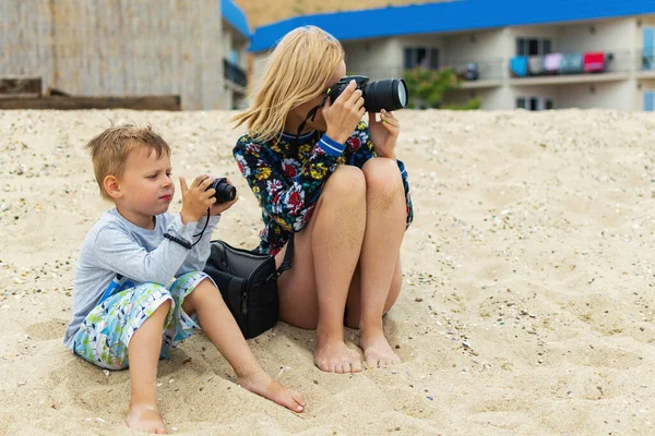 Mom and son are photographers. A woman and a young boy are holding a digital camera. Mother-child interaction, common hobby.