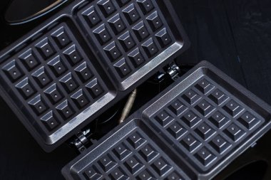 Siyah ahşap arka planda elektrikli waffle ızgarası. Belçika waffle 'ı yapmak için aygıt.