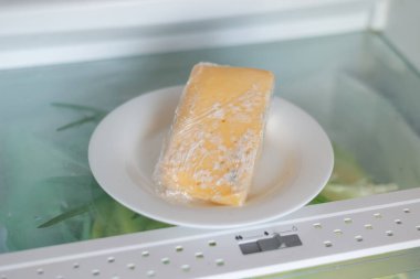 Moldy cheese wrapped in cling film in the refrigerator. Incorrect storage, spoiled product, expired concept. clipart
