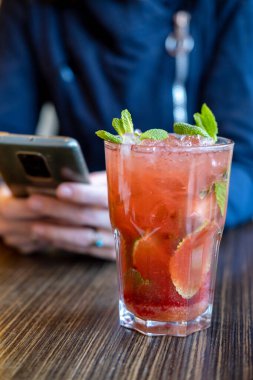 Mojito kokteyli ve kafede telefonu olan bir kadın. Dinlenmek, telefonda sohbet etmek, internet konseptini ödemek..