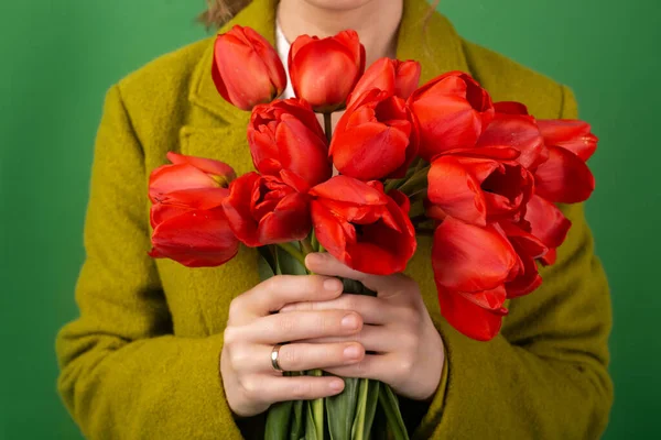 Kırmızı lale buketi, yeşil arka planda kadın ellerinde. Hediye, tatil, anneler günü konsepti.