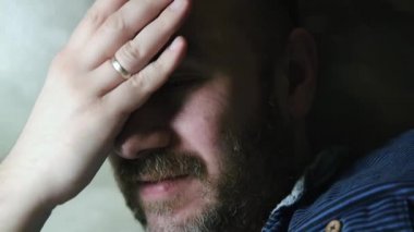 Tıraşsız, yorgun bir adamın yakın plan fotoğrafı eliyle başını ovuyor..