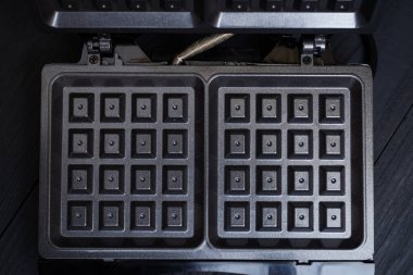 Siyah ahşap arka planda elektrikli waffle ızgarası. Belçika waffle 'ı yapmak için aygıt.