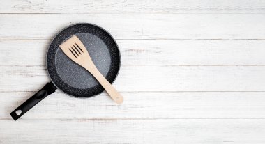 Çubuksuz seramik kaplama ve beyaz ahşap arka planda spatula ile kızartma tavası. Yapıştırmadan ya da yağsız yemek yapmak.
