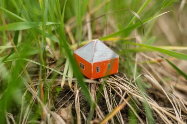 Güneşin altında yerde bir oyuncak ev. Gayrimenkul kavramı, şehir dışında yaşamak, kira, ipotek.