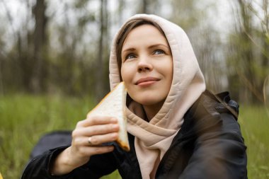 Yetişkin çekici bir kadın ormanda sandviç yiyor, park ediyor. Yürüyüşe çıkmış, yürüyüşe çıkmış..