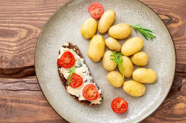 Haşlanmış patates ve tahıl ekmeği, mavi peynir ve ahşap bir tabakta domates. Vejetaryen yemeği..