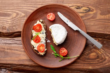 Tahta zemin üzerinde kil tabakta mavi peynirli ve kiraz domatesli tahıl ekmeği. Sağlıklı vejetaryen yemekleri.