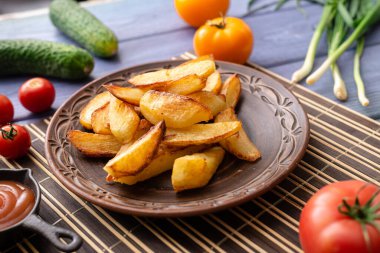 Masadaki tabakta farklı sebzelerle birlikte büyük parçalar halinde kızarmış patates..