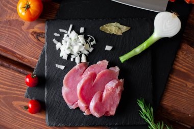 Dilimlenmiş çiğ hindi eti, doğranmış soğan, siyah bir arkaplanda..