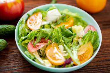 Tahta arka planda taze sebzelerden, otlardan ve domateslerden oluşan sağlıklı bir salata.