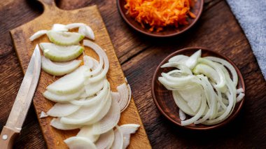 Koyu ahşap zemin üzerinde dilimlenmiş soğan ve havuç. Malzemeler, yemek hazırlığı..