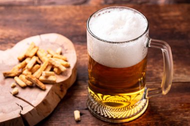 Ahşap arka planda bir bardak bira ve atıştırmalık..