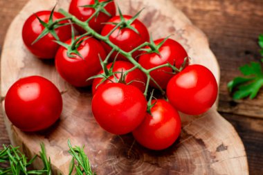 Kahverengi ahşap zemin üzerinde yeşillikler olan taze domatesler..