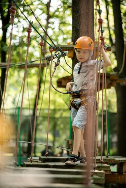 Çocuklar için ip parkı. Kanatlı genç bir çocuk engellere tırmanıyor. Çocuğun aktif spor eğlencesi.
