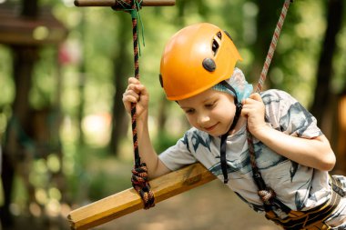 Dağ kenarındaki bir çocuk ve parmak arası terlik bir engelli parkurundan geçiyor. Bir çocuk için yazın aktif, sportif aktiviteler.