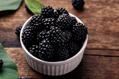 Taze böğürtlen böğürtlenleri ahşap bir arka planda beyaz bir kasede yakın planda.