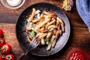 Eski ahşap bir zeminde, siyah bir tabakta fırında patates..