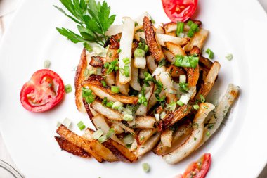 Beyaz tabakta kızarmış patates, yeşil soğan, maydanoz, beyaz ahşap arka planda domates..