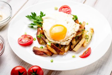 Yumurtalı kızarmış patates, otlar ve domatesler beyaz bir tabakta, ahşap arka planda..