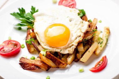 Yumurtalı kızarmış patates, otlar ve domatesler beyaz bir tabakta, ahşap arka planda..