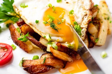 Yumurtalı kızarmış patates, sıvı sarısı, otlar ve domatesler beyaz tabakta..