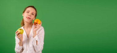 Beyaz gömlekli, orta yaşlı güzel bir kadın yeşil arka planda elmalar gösteriyor. Diyet, sağlıklı gıda, vejetaryenlik kavramı. Pankart. Metnin için yer.