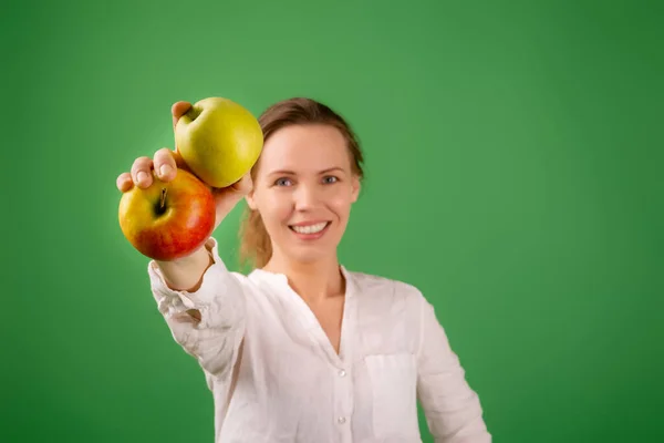 白いシャツに美しい中年女性が緑の背景にリンゴを示しています 健康食品 菜食主義の概念 — ストック写真