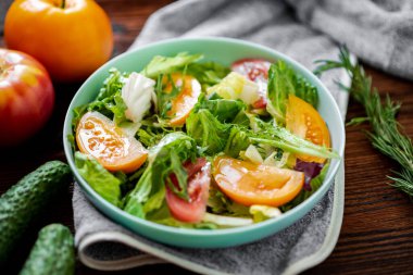 Tahta arka planda taze sebzelerden, otlardan ve domateslerden oluşan sağlıklı bir salata.