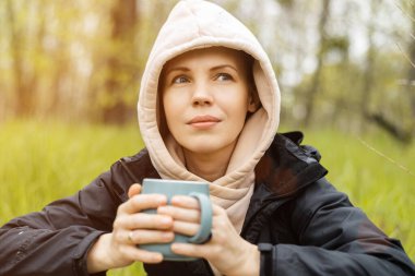 Ormanda fincanı olan bir kadın, serin havada yeşil arka bahçeye park ediyor. Doğada rahatlama, dinlenme..