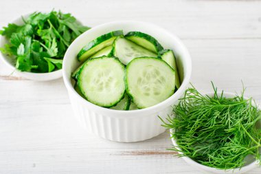 Taze doğranmış salatalık, maydanoz, beyaz ahşap arka planda dereotu. Salata malzemeleri. Vejetaryen gıda konsepti.