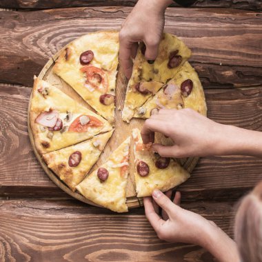 Eller koyu ahşap arka planda pizza parçalarını alır..
