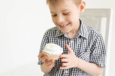 Gömlekli genç bir çocuk arka planda pasta yiyor. Tatlıların yemek sevinci.